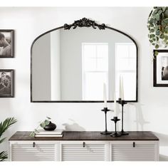 a mirror is hanging on the wall above a dresser with candles and other decor items