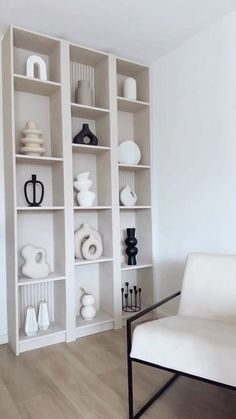 a white chair sitting in front of a bookshelf filled with vases