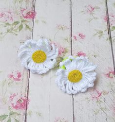 two crocheted white and yellow flowers sitting on top of a wooden floor