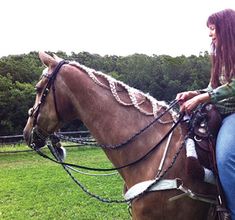 a woman riding on the back of a brown horse in a green field with trees