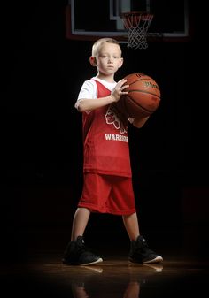 a young boy holding a basketball while standing on top of a basketball court in front of a hoop