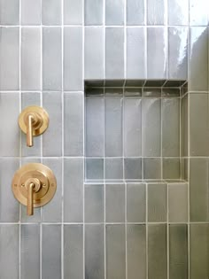 two gold faucets on the side of a white tiled shower