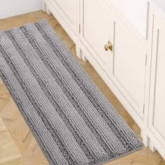 a gray rug sitting on top of a wooden floor next to a white cabinet and drawers