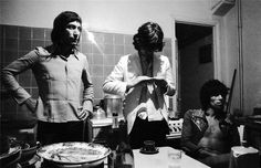 three people standing in a kitchen with food on the counter and one person holding a knife