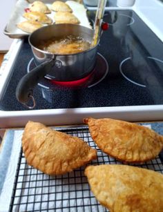 three pastries sitting on top of a stove next to a pan filled with food