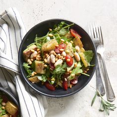 two black bowls filled with salad on top of a white and blue table cloth next to silverware