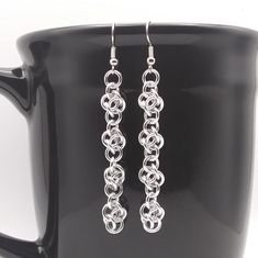 a pair of silver earrings sitting on top of a black coffee cup in front of a mug