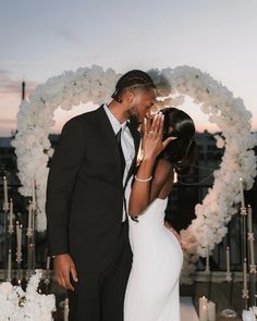 a bride and groom kissing in front of a wedding arch decorated with white flowers at sunset