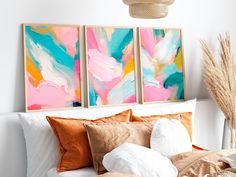 two paintings on the wall above a bed with pillows and blankets in front of it