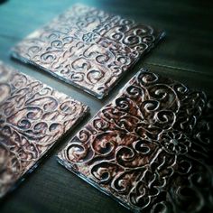 four square metal coasters sitting on top of a wooden table next to each other