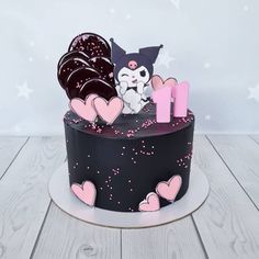 a cake decorated with pink and black icing on top of a wooden table next to a white wall