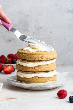 a person is cutting into a stack of cookies with whipped cream and berries around them