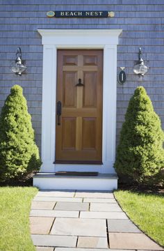 the front door to beach nest is flanked by two small trees and brick walkways