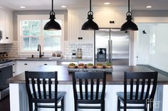 a kitchen with three black chairs sitting at the center of the counter and two lights hanging from the ceiling