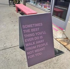 a purple sign sitting on the side of a street next to a sidewalk with a pink bench