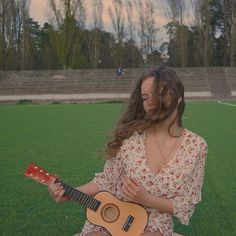 a woman sitting in the grass playing an acoustic guitar