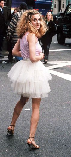 a woman in a white tutu walking down the street with other people behind her