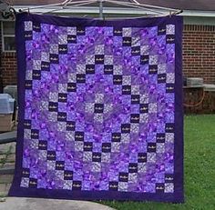 a purple and black quilt hanging from a clothes line in front of a brick house