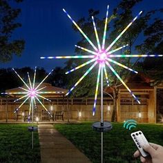 a hand holding a remote control in front of a star shaped light up decoration on top of a lawn