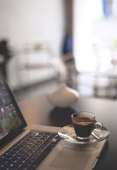 a laptop computer sitting on top of a wooden table next to a cup of coffee