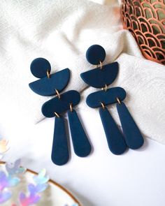 two pairs of blue earrings sitting on top of a white cloth next to a plate