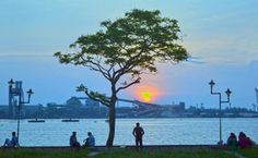 people sitting and standing near the water at sunset