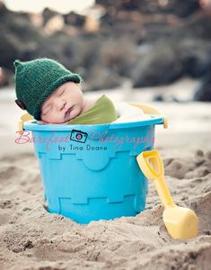 a baby laying in a blue bucket on the beach