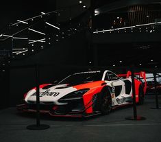 an orange and white sports car on display in a showroom with black lighting overhead