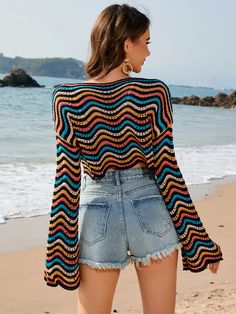 a woman standing on top of a beach next to the ocean wearing shorts and a sweater