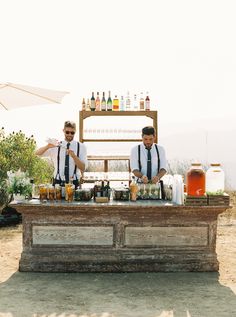 two men in ties are making drinks at an outdoor bar with bottles on the counter