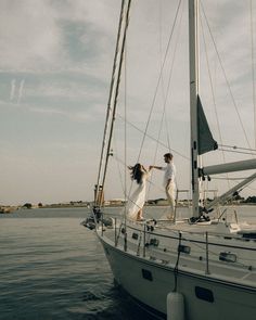 a man and woman standing on the deck of a sailboat