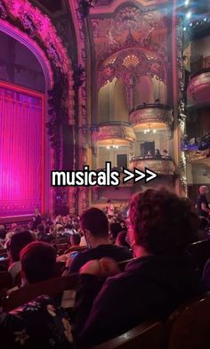 an auditorium filled with people sitting and standing in front of a pink curtain that reads musicals > >