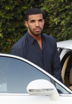 a man standing in front of a car with his hand on the door handle and looking at the camera