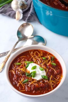 a bowl of chili soup with sour cream on top and spoons next to it