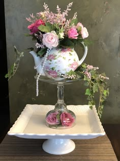 a white tea pot with pink flowers in it sitting on a plate next to a vase