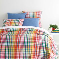 a bed with colorful plaid comforter and pillows on top of it, next to a plant