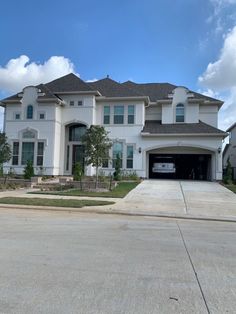 a large white house with a car parked in the driveway and two garages on each side