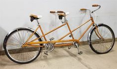 an orange bicycle parked next to a white wall in a room with concrete flooring