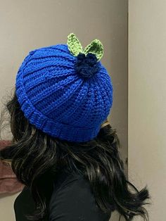 a woman wearing a blue knitted hat with a green leaf on it's back