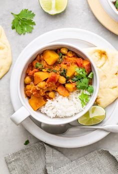 a white bowl filled with curry and rice next to pita bread, lime wedges and cilantro