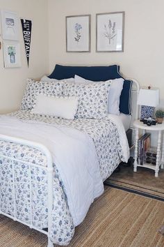 a white bed with blue and white comforter in a bedroom next to pictures on the wall