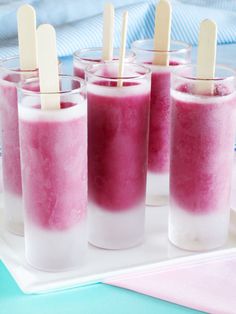 four glasses filled with ice cream and popsicle sticks on a tray next to a pink napkin