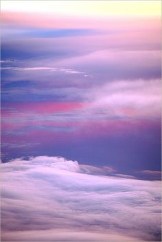 an airplane flying in the sky with clouds below it and some pinks and blue