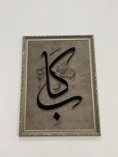 an arabic calligraphy is hanging on the wall in front of a white background with silver frame