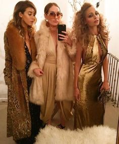 three beautiful women standing next to each other in front of a white wall holding a cell phone