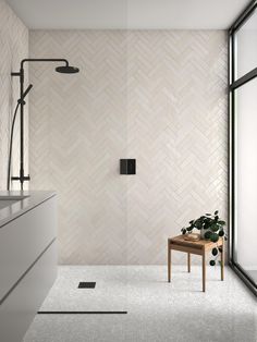 a modern bathroom with white tile walls and flooring, along with a plant on the side of the bathtub