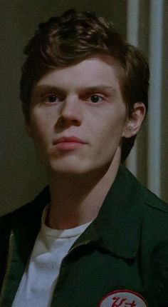 a young man in a green jacket looking at the camera with an intense look on his face