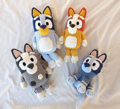 three crocheted stuffed animals sitting on top of a white bed sheet, with one dog and the other cat