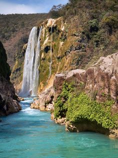 a large waterfall is in the middle of a river with blue water and green vegetation