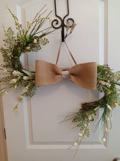 a bow tie hanging on the front door with greenery and scissors attached to it